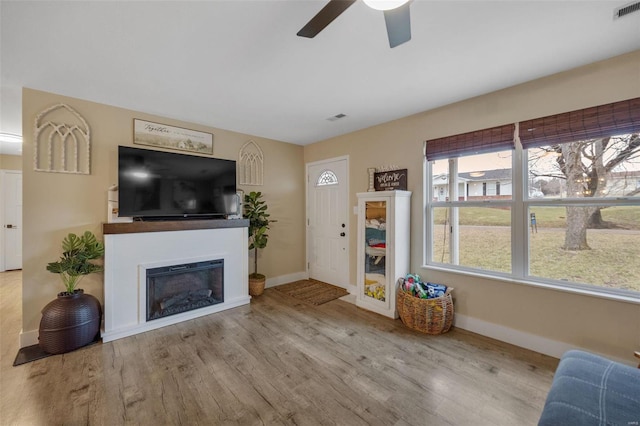 living area featuring visible vents, a fireplace, baseboards, and wood finished floors