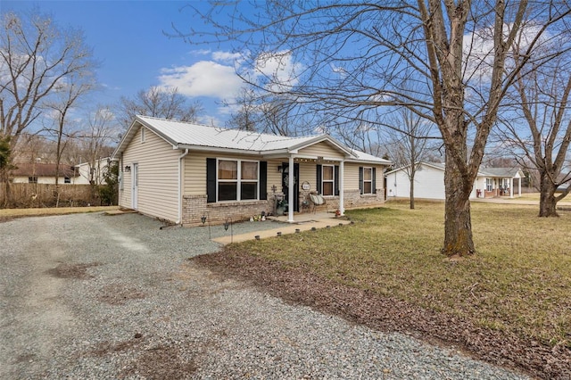 view of front facade with metal roof, brick siding, a front yard, and gravel driveway