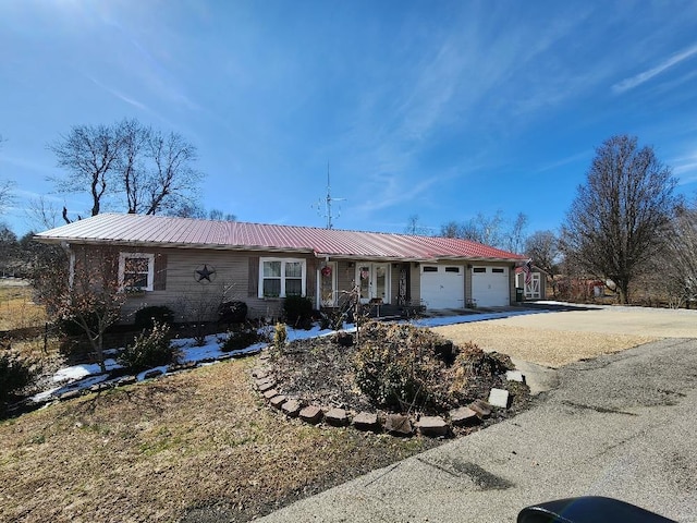 ranch-style home with metal roof, an attached garage, and driveway