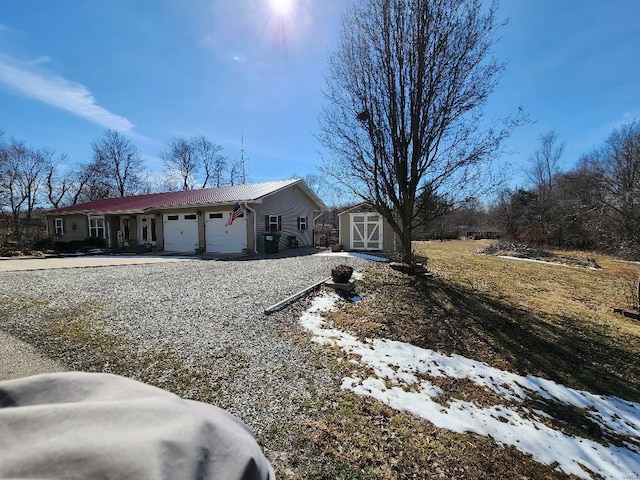 single story home featuring an outbuilding, a storage unit, an attached garage, metal roof, and driveway