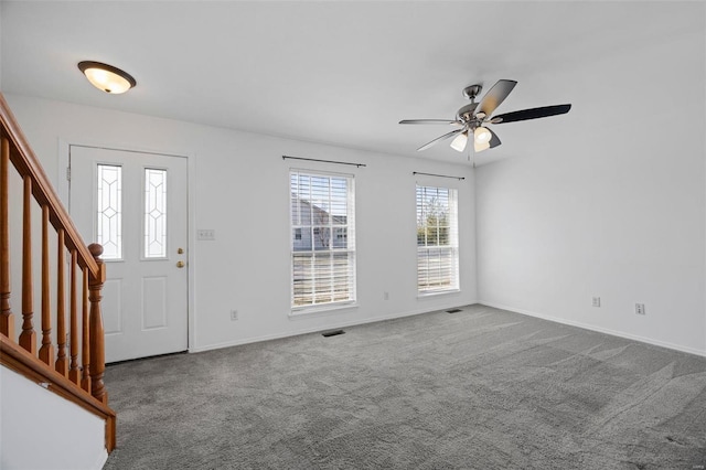 carpeted foyer entrance with baseboards, visible vents, stairway, and a ceiling fan