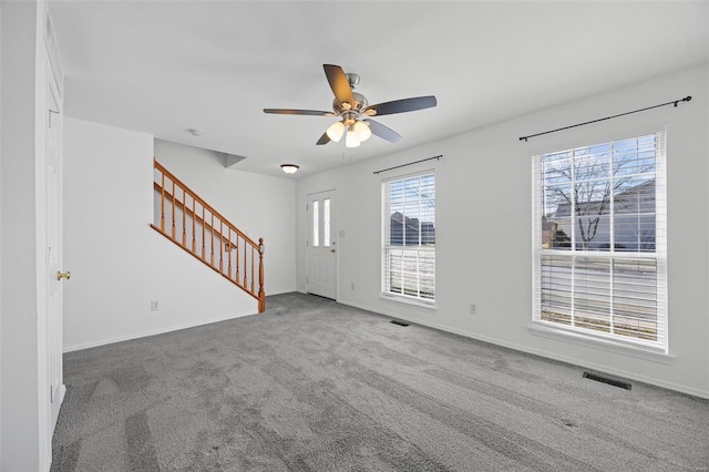 unfurnished living room with ceiling fan, carpet flooring, visible vents, baseboards, and stairway