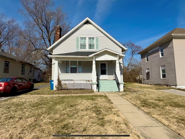 bungalow featuring covered porch, a chimney, and a front yard