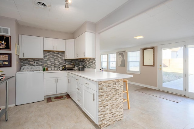 kitchen featuring washer / clothes dryer, visible vents, a peninsula, and backsplash