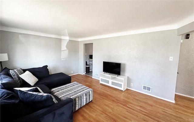 living room featuring a textured wall, wood finished floors, visible vents, and baseboards