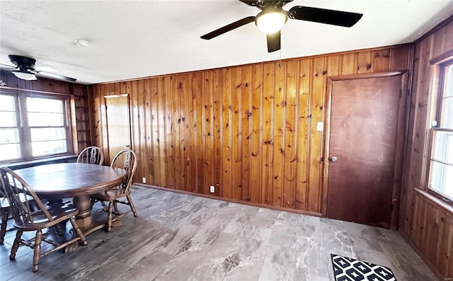 dining room featuring a textured ceiling, a ceiling fan, and wooden walls