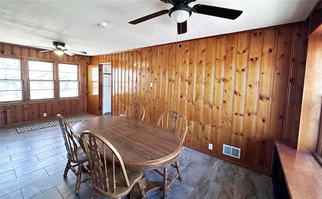 dining room with wood walls, ceiling fan, visible vents, and a textured ceiling