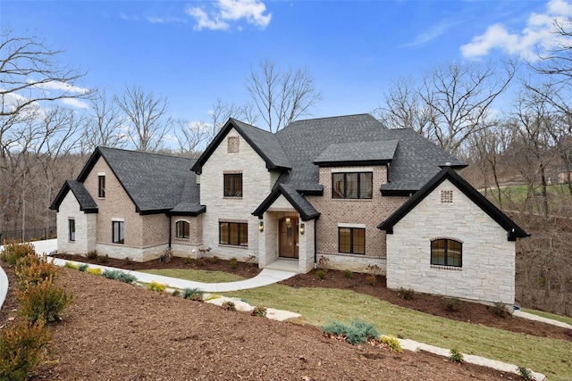 french provincial home featuring a shingled roof, brick siding, and a front lawn