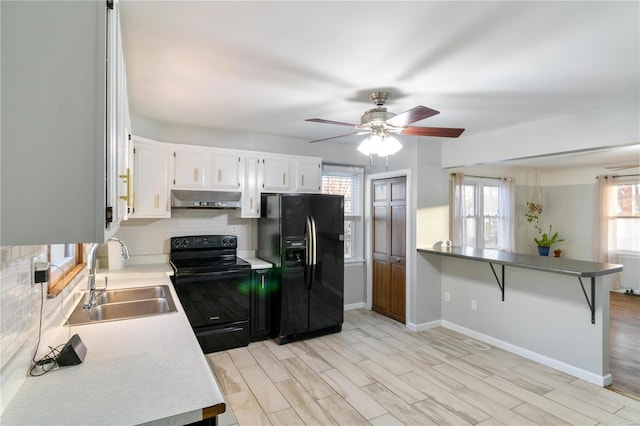 kitchen featuring backsplash, under cabinet range hood, light wood-style flooring, black appliances, and a sink