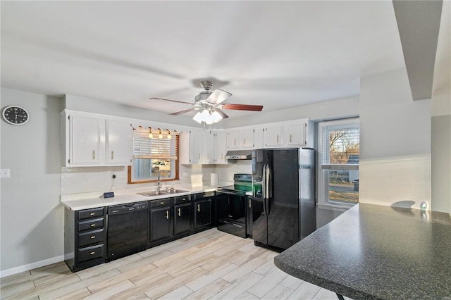 kitchen featuring black appliances, a sink, under cabinet range hood, dark cabinetry, and white cabinets