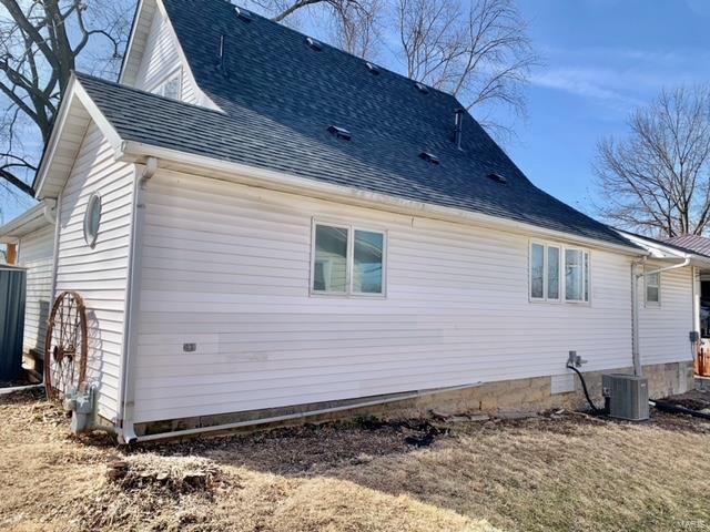 view of side of property featuring a shingled roof and central AC