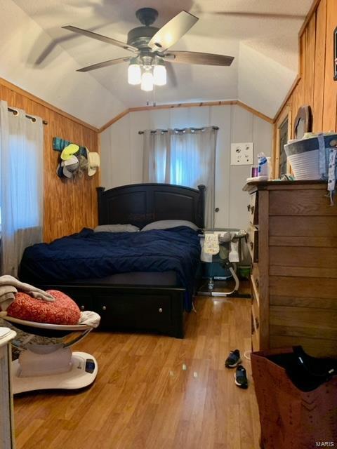 bedroom featuring lofted ceiling, wood walls, a ceiling fan, and wood finished floors