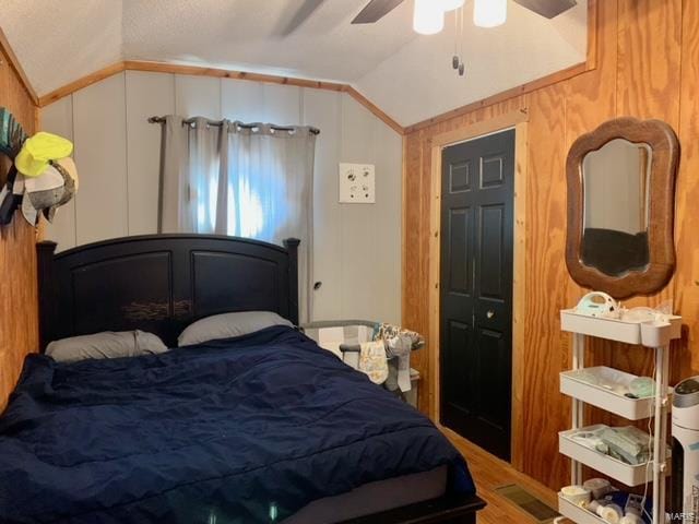 bedroom featuring lofted ceiling, wooden walls, and a ceiling fan