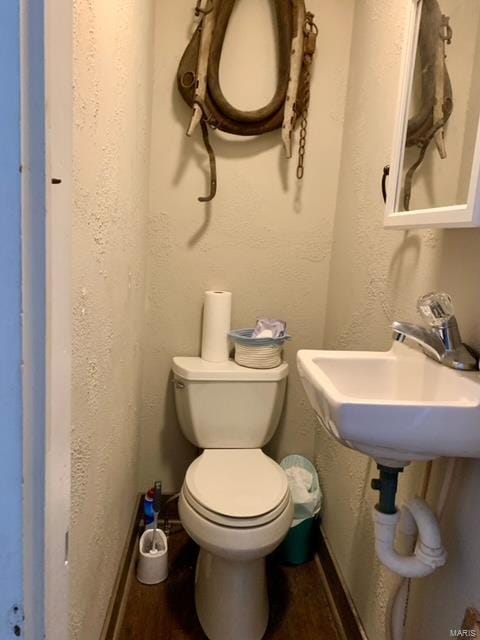 bathroom with toilet, a sink, wood finished floors, and a textured wall