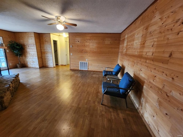 living area with visible vents, a ceiling fan, wood finished floors, a textured ceiling, and wood walls