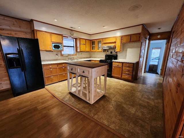 kitchen featuring a textured ceiling, under cabinet range hood, wood finished floors, brown cabinets, and black appliances