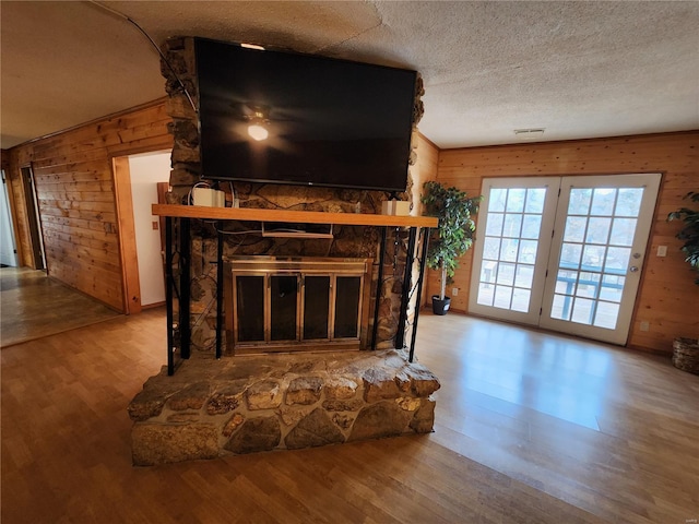 living room with a stone fireplace, wood walls, and wood finished floors