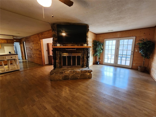 unfurnished living room featuring wooden walls, a ceiling fan, wood finished floors, a textured ceiling, and a fireplace