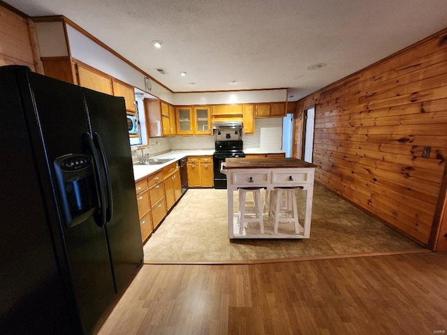 kitchen featuring wood walls, a sink, light wood-type flooring, black appliances, and glass insert cabinets