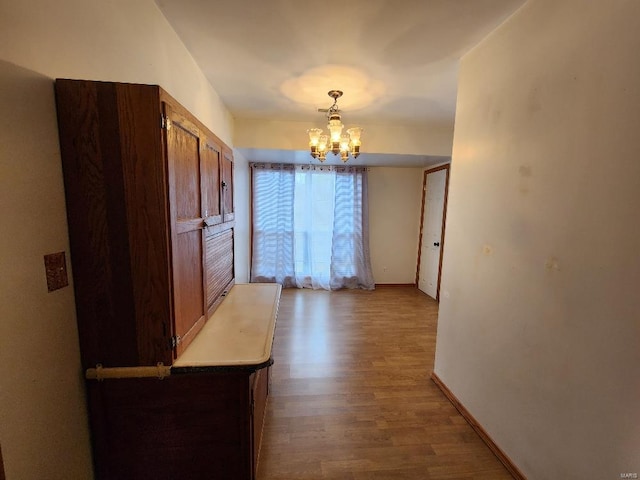 unfurnished dining area with an inviting chandelier, baseboards, and wood finished floors