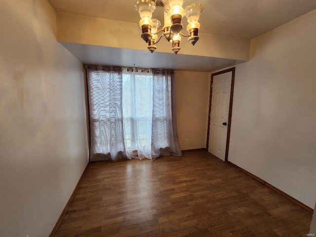 spare room featuring a notable chandelier, baseboards, and wood finished floors