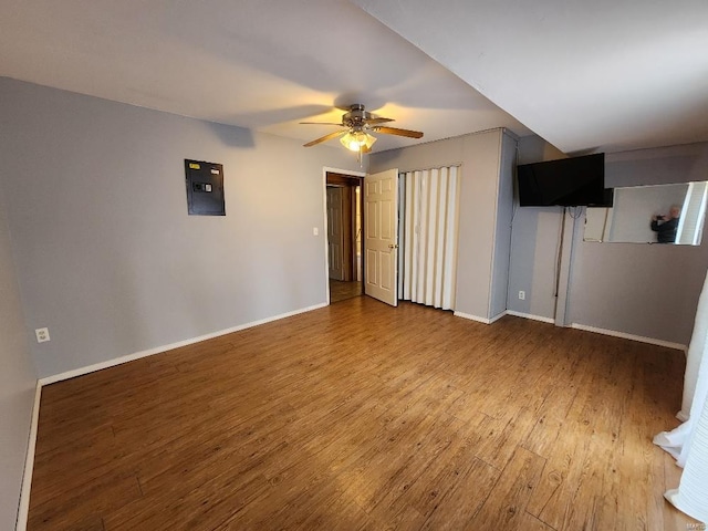 unfurnished living room featuring electric panel, ceiling fan, baseboards, and wood finished floors