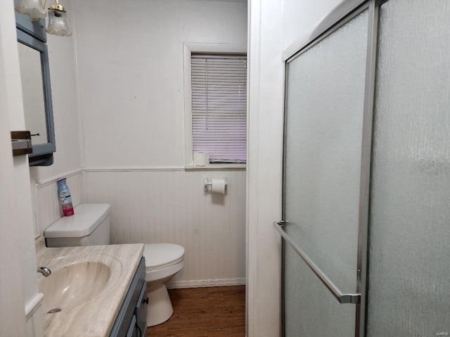 full bath featuring a wainscoted wall, toilet, vanity, a shower stall, and wood finished floors