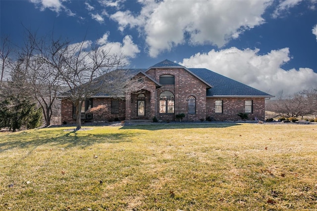 french country home featuring roof with shingles, brick siding, and a front lawn