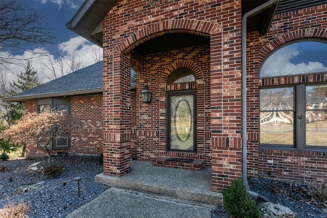 entrance to property with a shingled roof and brick siding