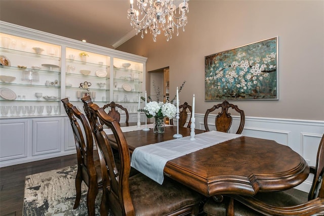 dining area with a wainscoted wall, dark wood-style floors, an inviting chandelier, crown molding, and a decorative wall