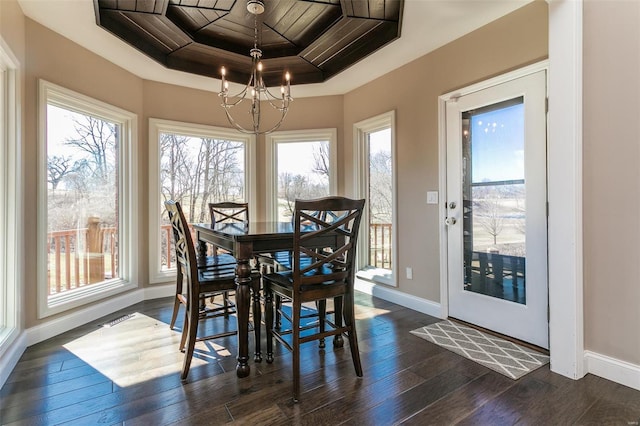 dining room featuring a chandelier, dark wood-style flooring, a raised ceiling, and baseboards