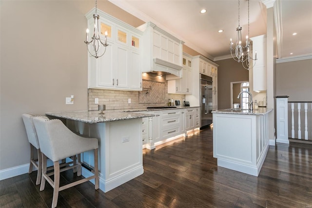 kitchen featuring built in refrigerator, a peninsula, glass insert cabinets, and a notable chandelier