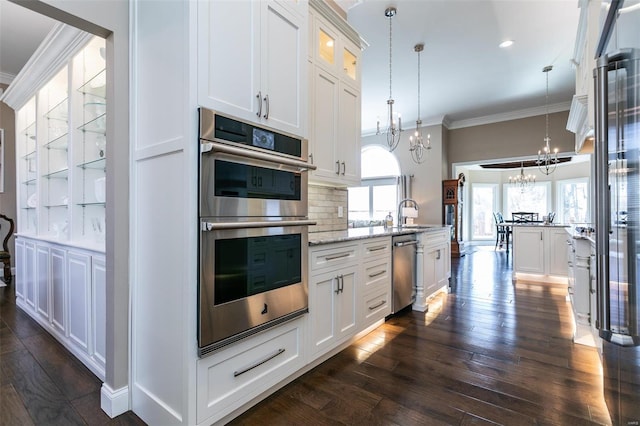 kitchen with dark wood finished floors, crown molding, a notable chandelier, appliances with stainless steel finishes, and a peninsula