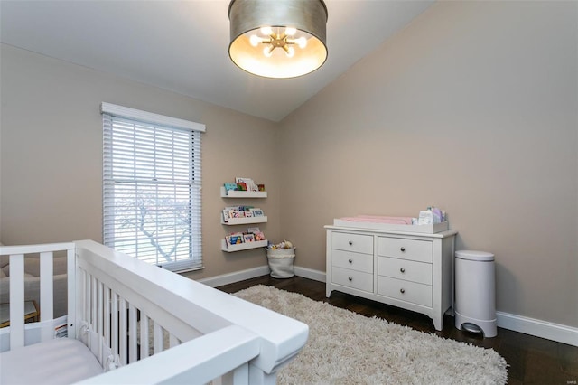 bedroom featuring a nursery area, dark wood-style floors, baseboards, and vaulted ceiling