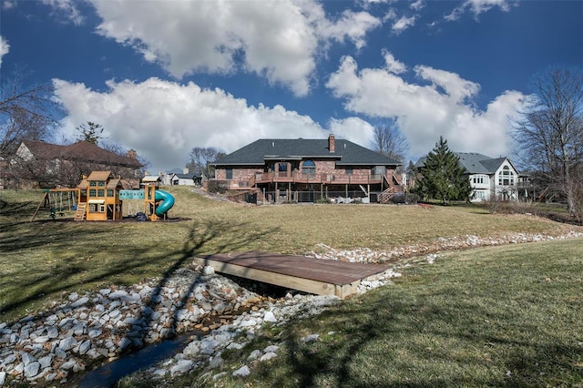 rear view of property with a lawn, a playground, and a wooden deck