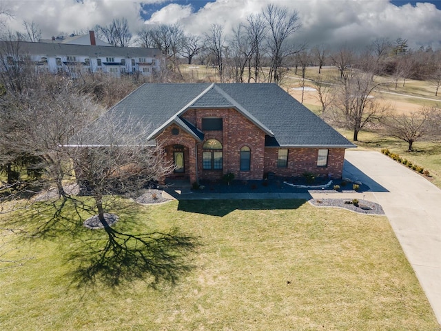 traditional home featuring a shingled roof, brick siding, and a front lawn