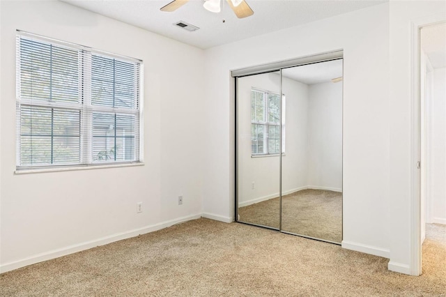 unfurnished bedroom with a closet, light colored carpet, visible vents, and multiple windows