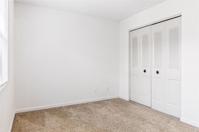 unfurnished bedroom with carpet, a closet, a textured ceiling, and baseboards