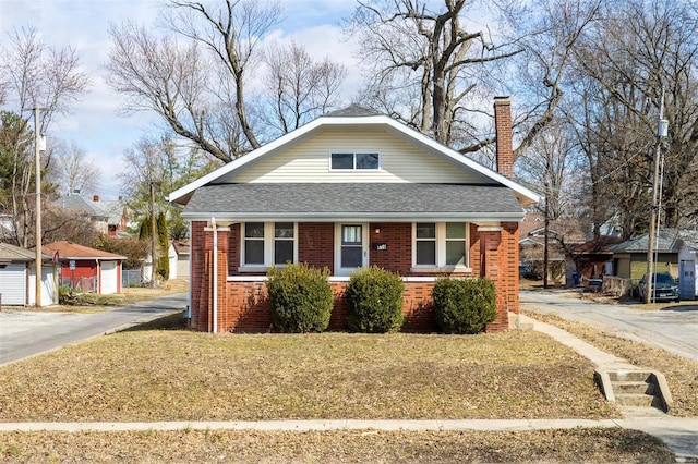 bungalow-style home featuring roof with shingles, a chimney, and brick siding