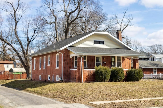 view of property exterior with brick siding, a yard, a chimney, a shingled roof, and fence