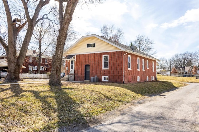 view of front of property featuring brick siding, fence, a front lawn, and central AC unit