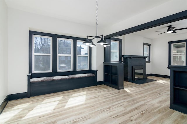 interior space featuring a brick fireplace, a ceiling fan, baseboards, and wood finished floors