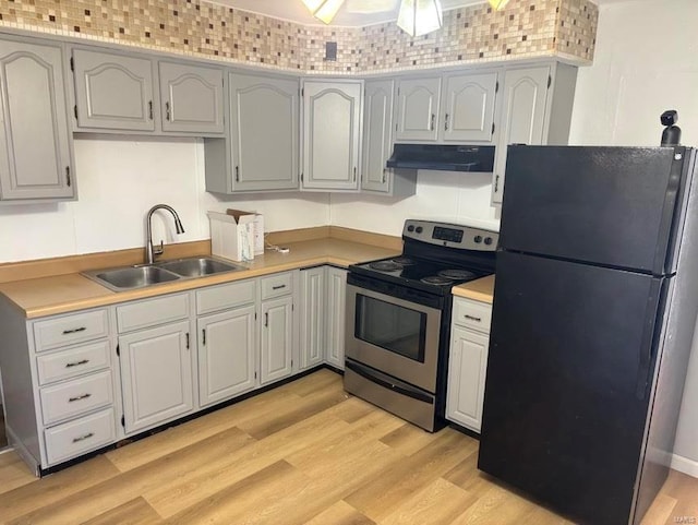 kitchen featuring light wood-style floors, freestanding refrigerator, stainless steel electric range, under cabinet range hood, and a sink