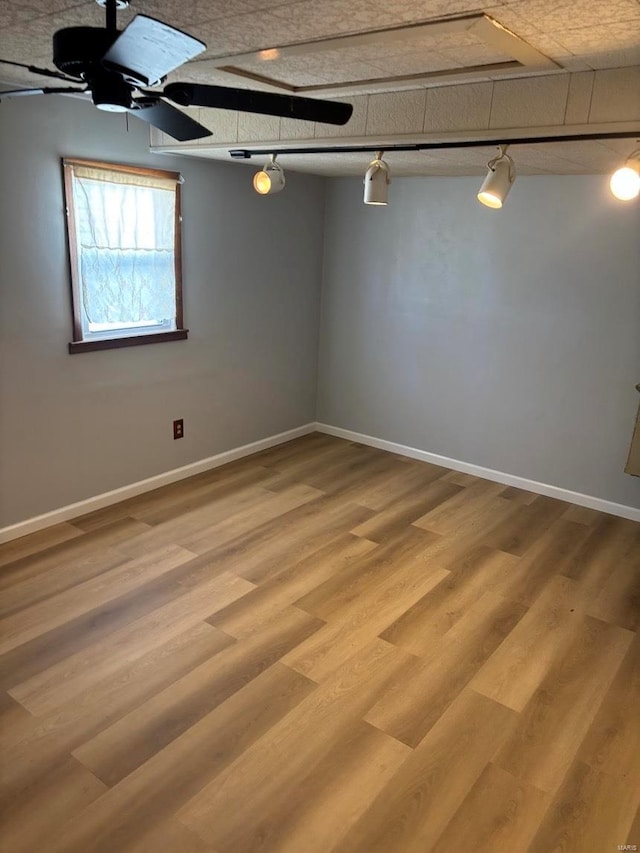 empty room featuring light wood-style floors, rail lighting, ceiling fan, and baseboards