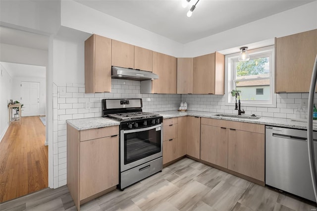 kitchen featuring light brown cabinetry, light stone countertops, under cabinet range hood, a sink, and appliances with stainless steel finishes