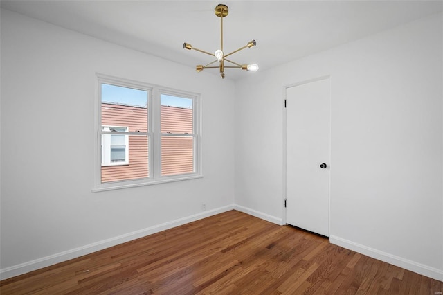 unfurnished room with an inviting chandelier, baseboards, and wood finished floors