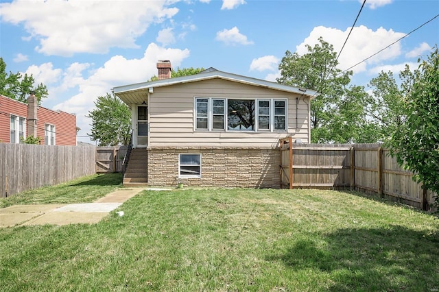 rear view of house with a yard, a chimney, a fenced backyard, and stone siding