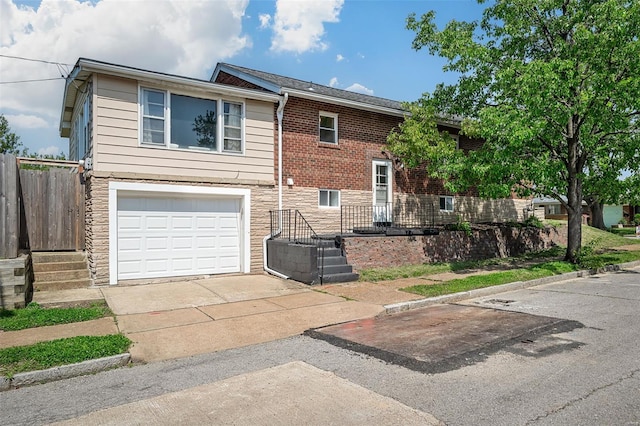 split foyer home featuring fence, an attached garage, driveway, and stone siding