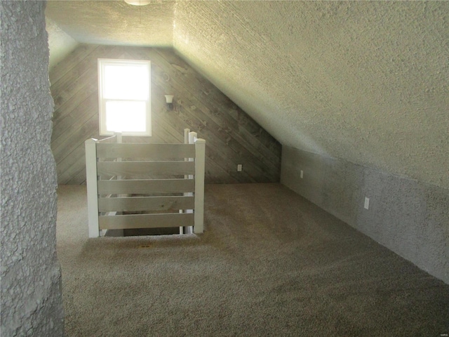 additional living space featuring vaulted ceiling, carpet flooring, wood walls, and a textured ceiling