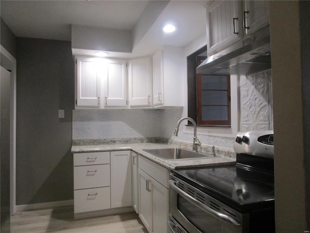 kitchen with tasteful backsplash, under cabinet range hood, double oven range, white cabinets, and a sink